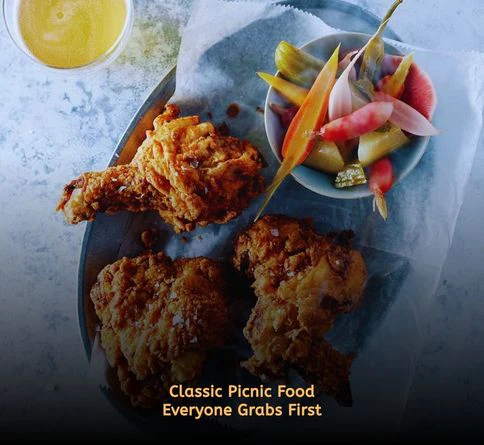 Crispy cold fried chicken pieces arranged in a picnic basket on a checkered blanket outdoors