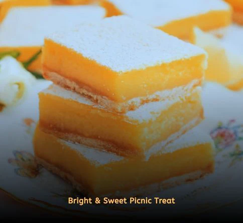 Homemade lemon bars dusted with powdered sugar on a picnic blanket.