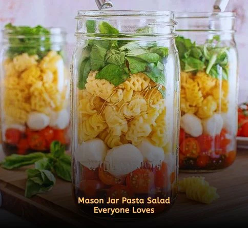 Colorful pasta salad layered in glass mason jars with vegetables, cheese, and vinaigrette for picnic meals.