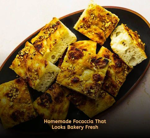 Golden herb focaccia bread topped with rosemary and thyme on a rustic picnic blanket.
