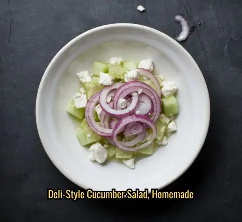  Red onion cucumber feta salad with thin onion rings and feta crumbles in a white bowl on slate.

