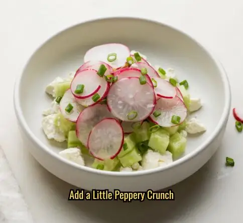 Radish cucumber feta salad with paper-thin radish slices and fresh chives in a white bowl.
