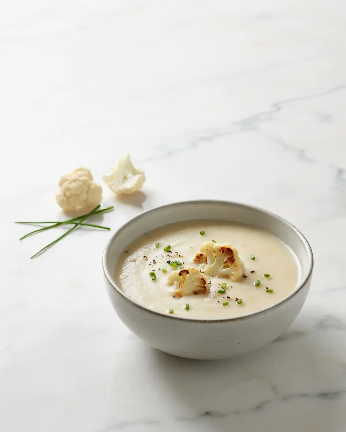 Creamy cauliflower potato soup topped with roasted cauliflower, chives, and black pepper.
