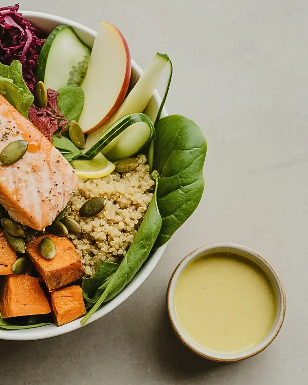 Salmon sweet potato harvest bowl with quinoa, greens, apple, cucumber, and pumpkin seeds.